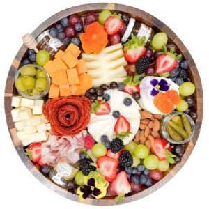 Small charcuterie board by Fork and Flare with Brie, Prairie Breeze White Cheddar, Boursin, Manchego, Rustic Red Cheddar, smoked salami, prosciutto, fresh berries, olives, honey, and crackers on an acacia wood board in Orange County.