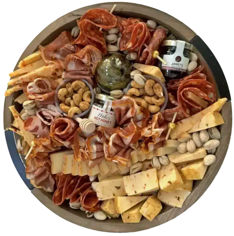 A 12-inch round Some Like it Hot Spicy Charcuterie Board featuring an array of bold ingredients—chili garlic cashews, cajun cheddar, cheddar with scotch bonnet, chili red peppers, smoked spicy gouda, spicy cornichons, pistachios, sweet and spicy prosciutto, hot sopressata salami, uncured hot copa, and uncured chorizo with paprika and oregano—served with chili crackers, jalapeno jam, and Mikes Hot Honey with honey dippers.