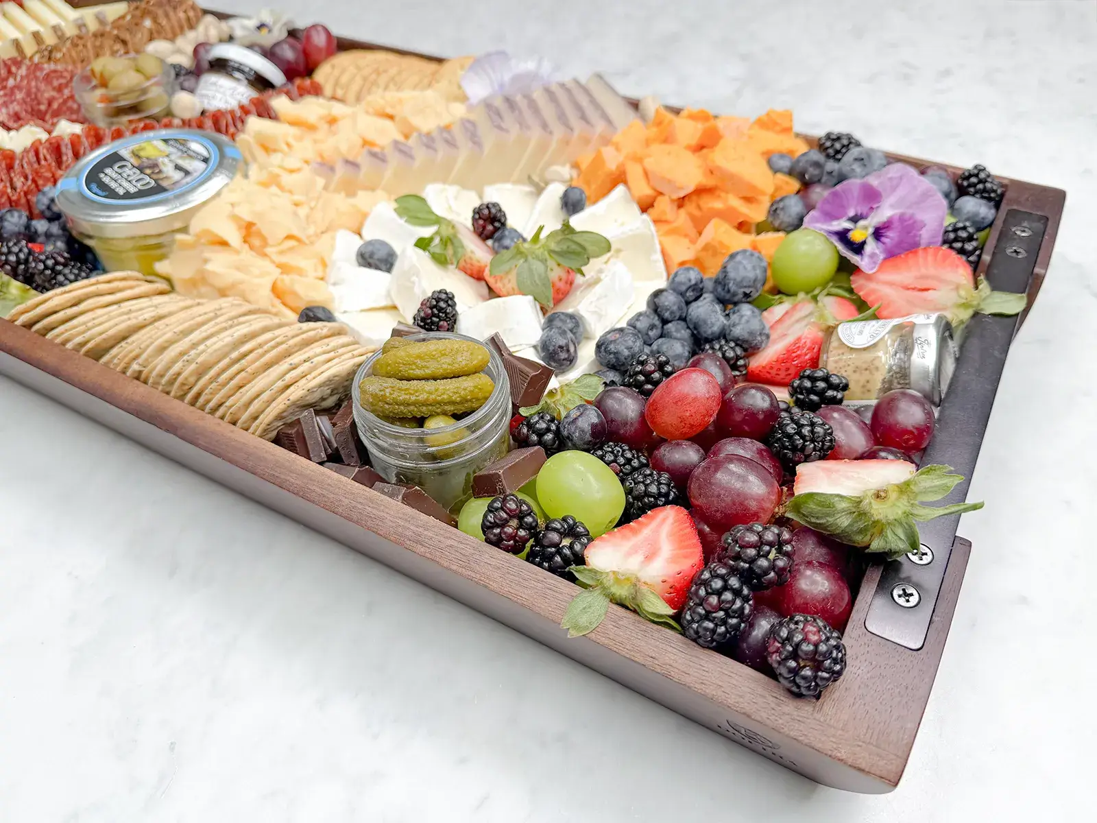 Grab and Graze charcuterie board by Fork and Flare in Irvine, Orange County California featuring over six pounds of gourmet cheeses, hand cut imported salami roses, fresh strawberries and grapes, artisan crackers, pistachios, olives, jam, honey and stone ground mustard for upscale party catering serving 36 to 42 guests.