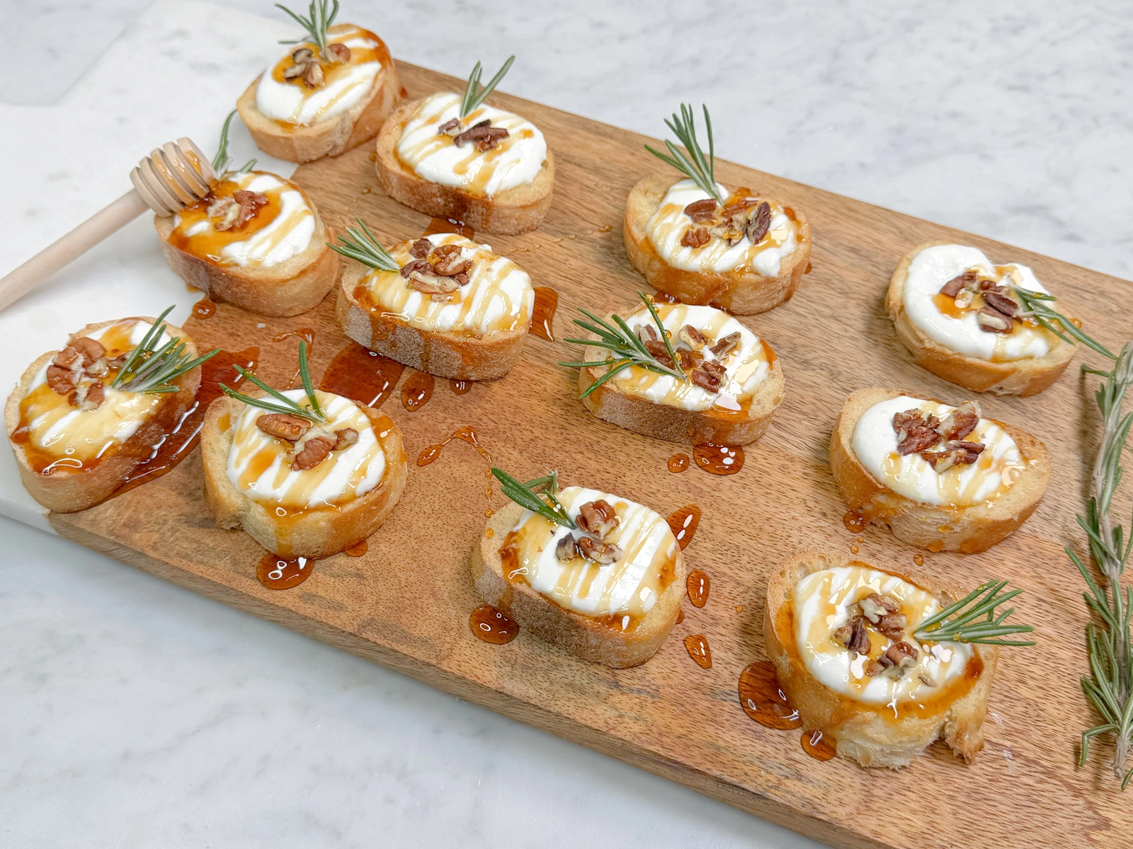 Whipped feta canapes on toasted baguette topped with crushed candied pecans, a rosemary sprig, and a honey drizzle, presented as elegant gourmet canapes by Fork and Flare in Orange County