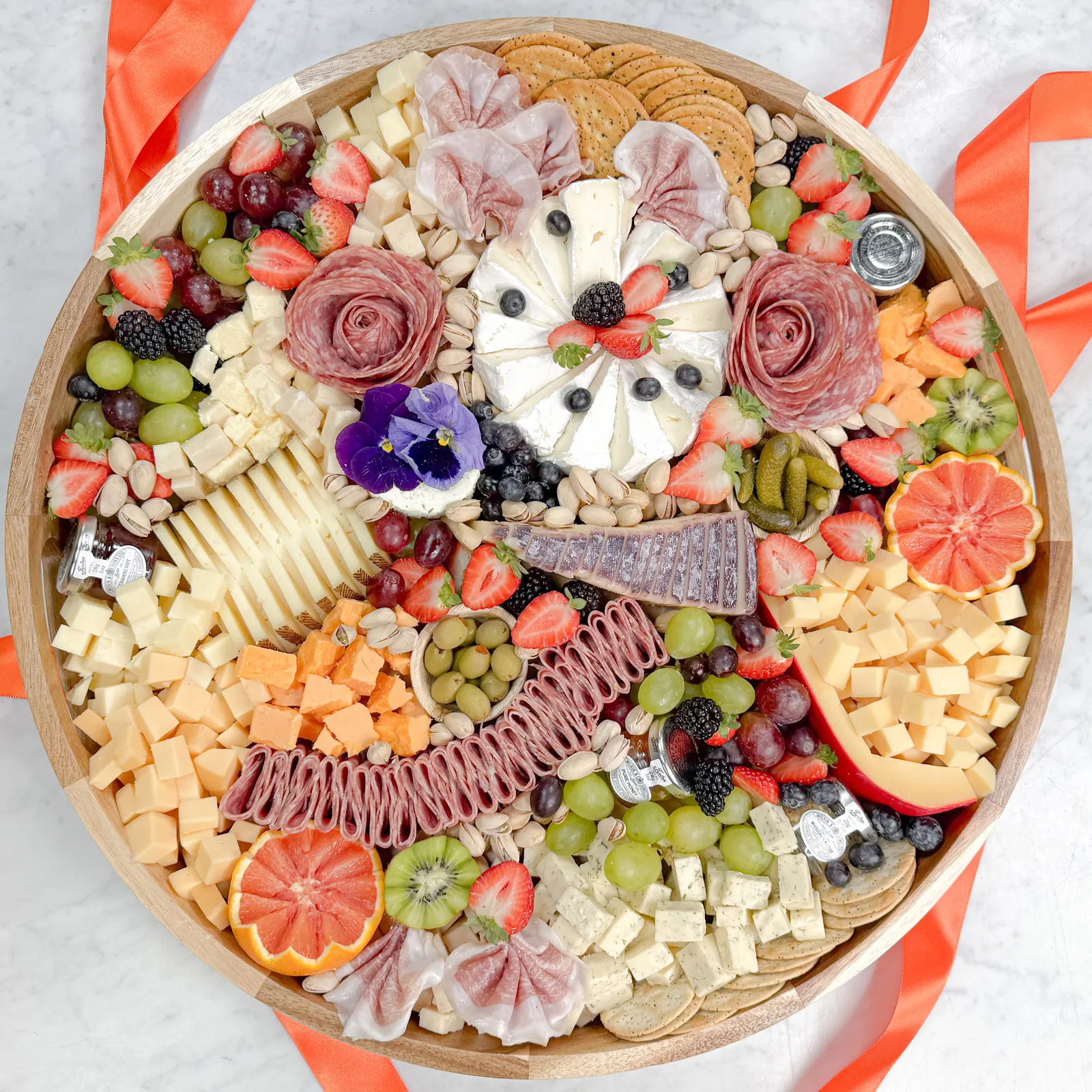 Best charcuterie boards in Orange County is showcased in this Fork and Flare image, featuring a handcrafted acacia wood charcuterie board by Fork and Flare with artisan cheeses, salami roses, prosciutto, fresh berries, grapes, olives, pistachios, and crackers arranged for luxury charcuterie catering and gourmet events in Orange County.
